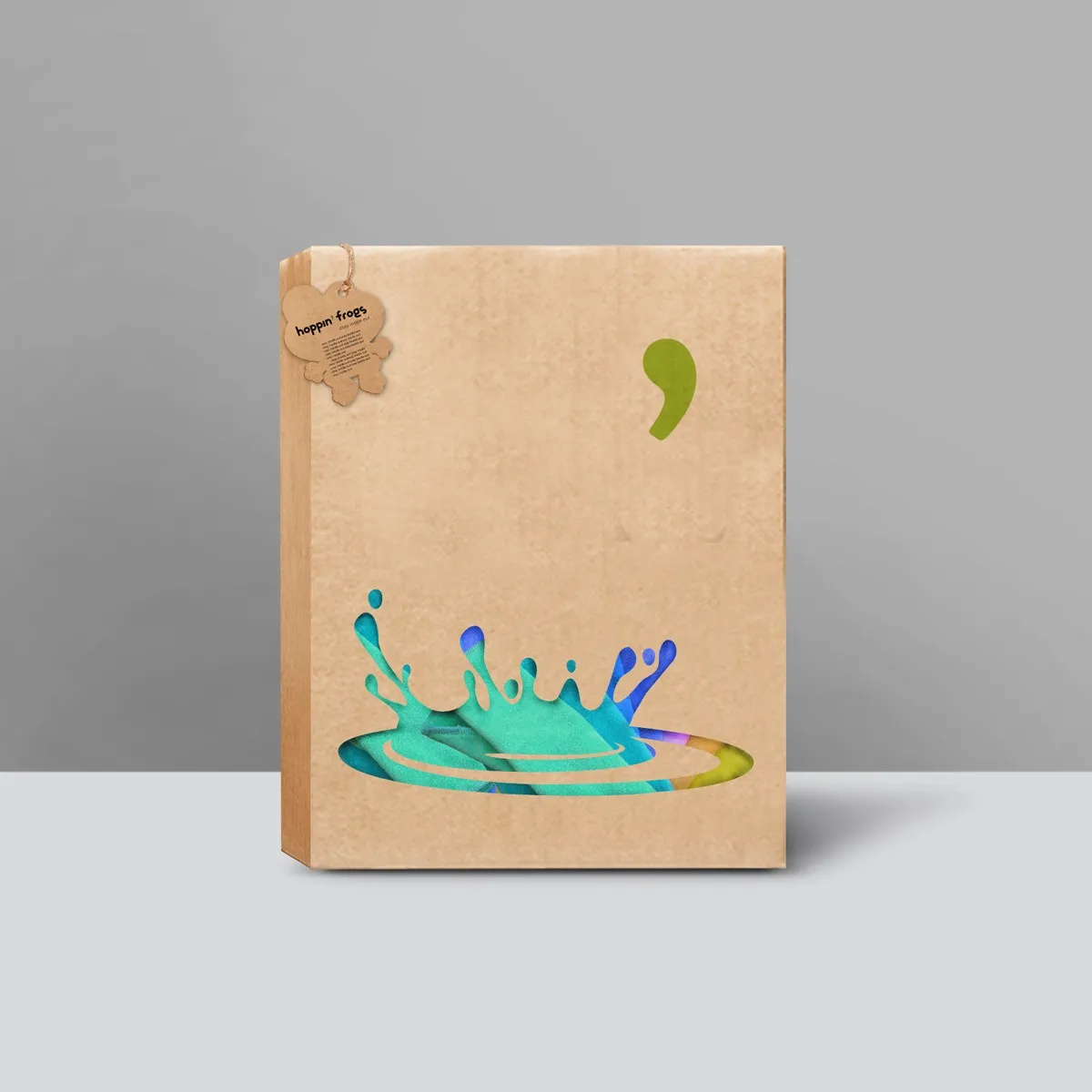 hoppin' frogs kraft gift box (comma variant) — lime-green apostrophe/comma mark top-right, die-cut water-splash window at base revealing colourful fabric inside; frog hang tag at left