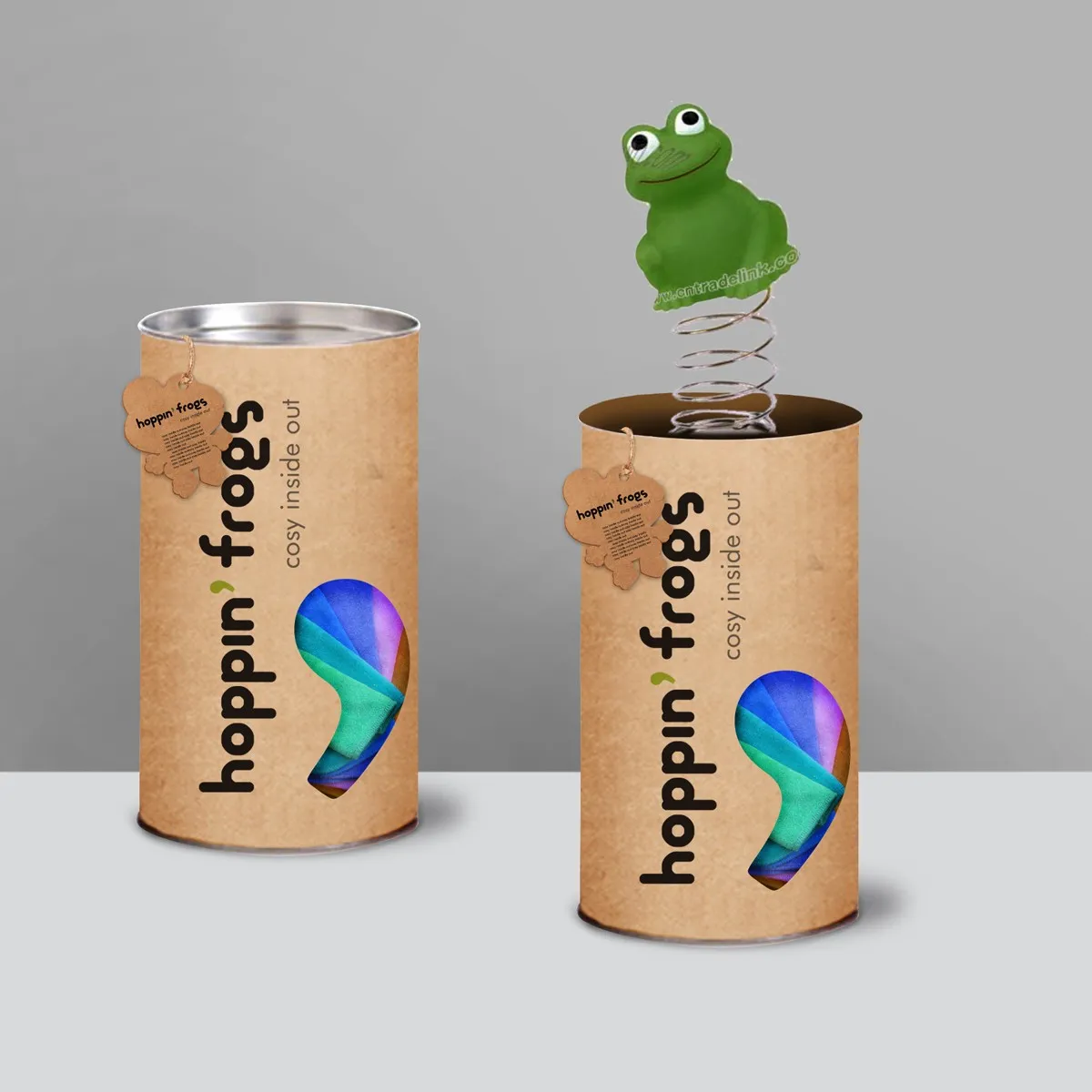 hoppin' frogs — two kraft cylinder tubes side by side; right tube has a jack-in-a-box green frog on a spring popping from the open top, demonstrating packaging as play