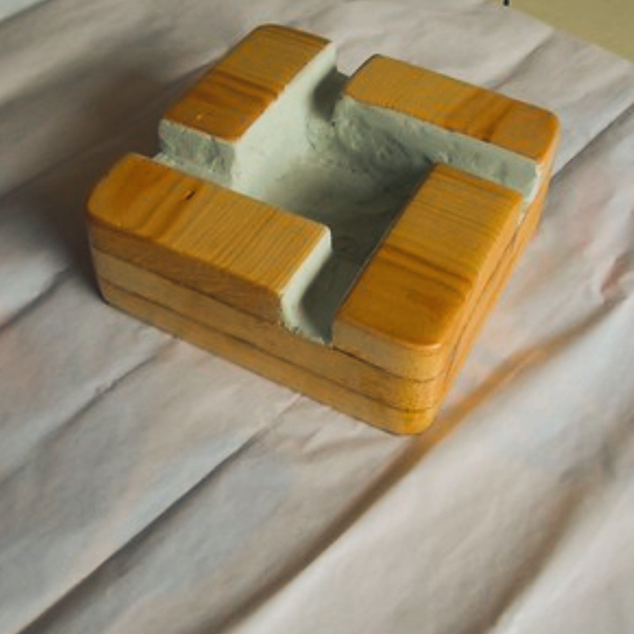 Plumber's ashtray — cross-shaped wooden frame stained yellow, filled with cast concrete in the centre hollow