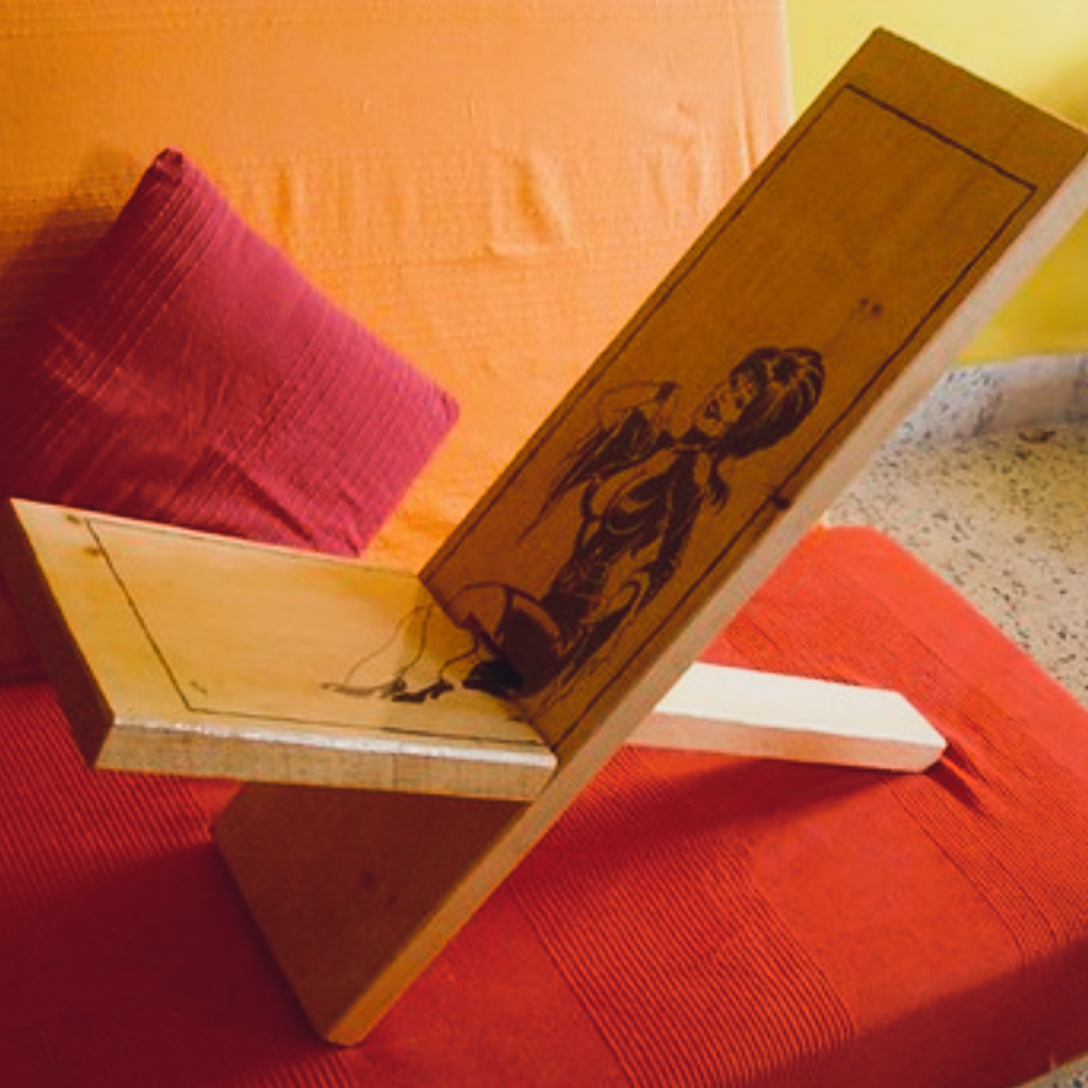 Low angled wooden book or tablet holder with a printed illustration of a reclining figure on the surface