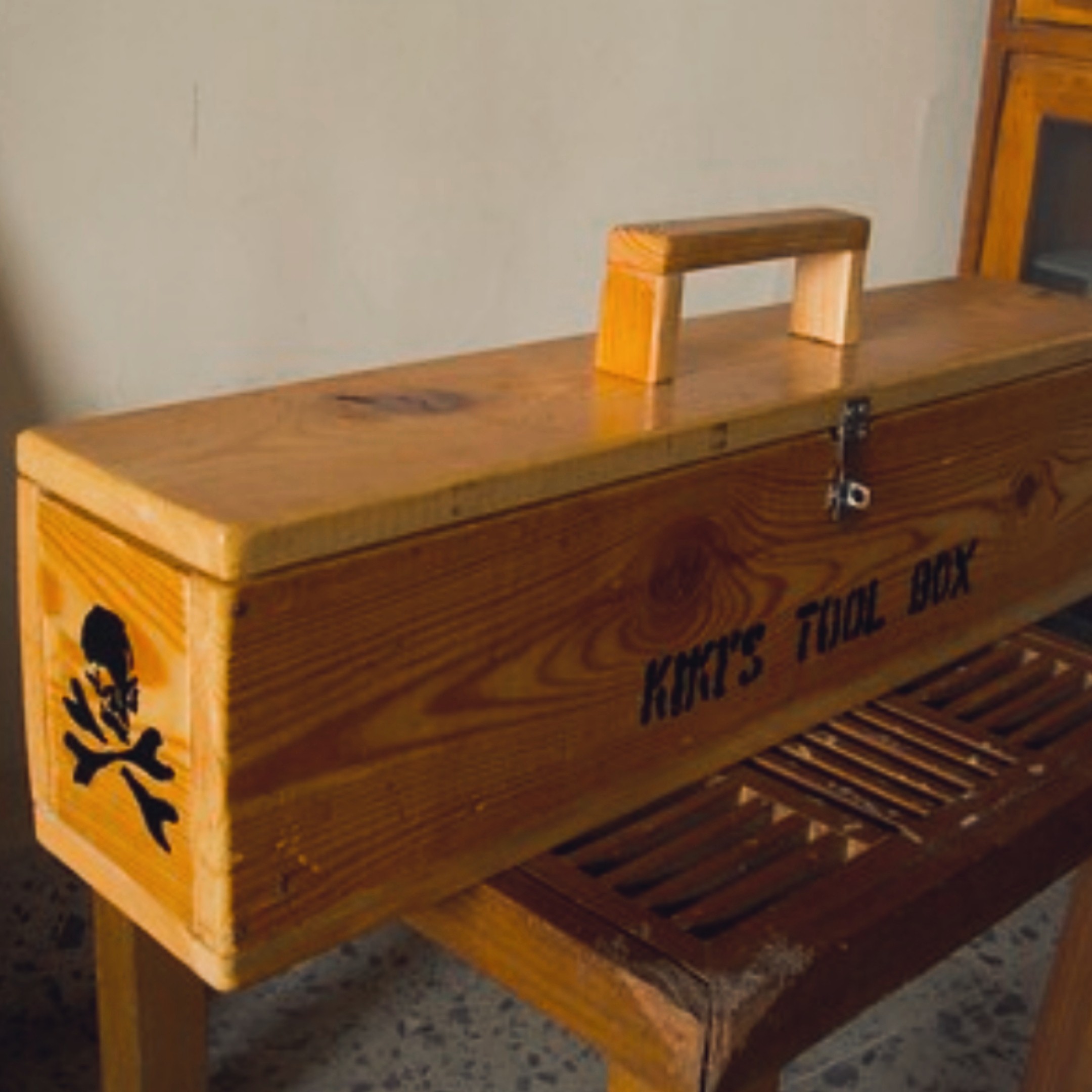"Kiki's Tool Box" — long pinewood tool chest with carry handle, metal latch, and hand-painted skull-and-crossbones logo