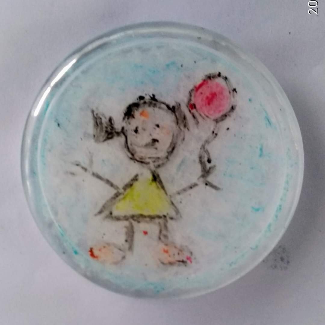 Round resin coaster with a child's drawing of a girl in pigtails holding a red balloon, blue wash background