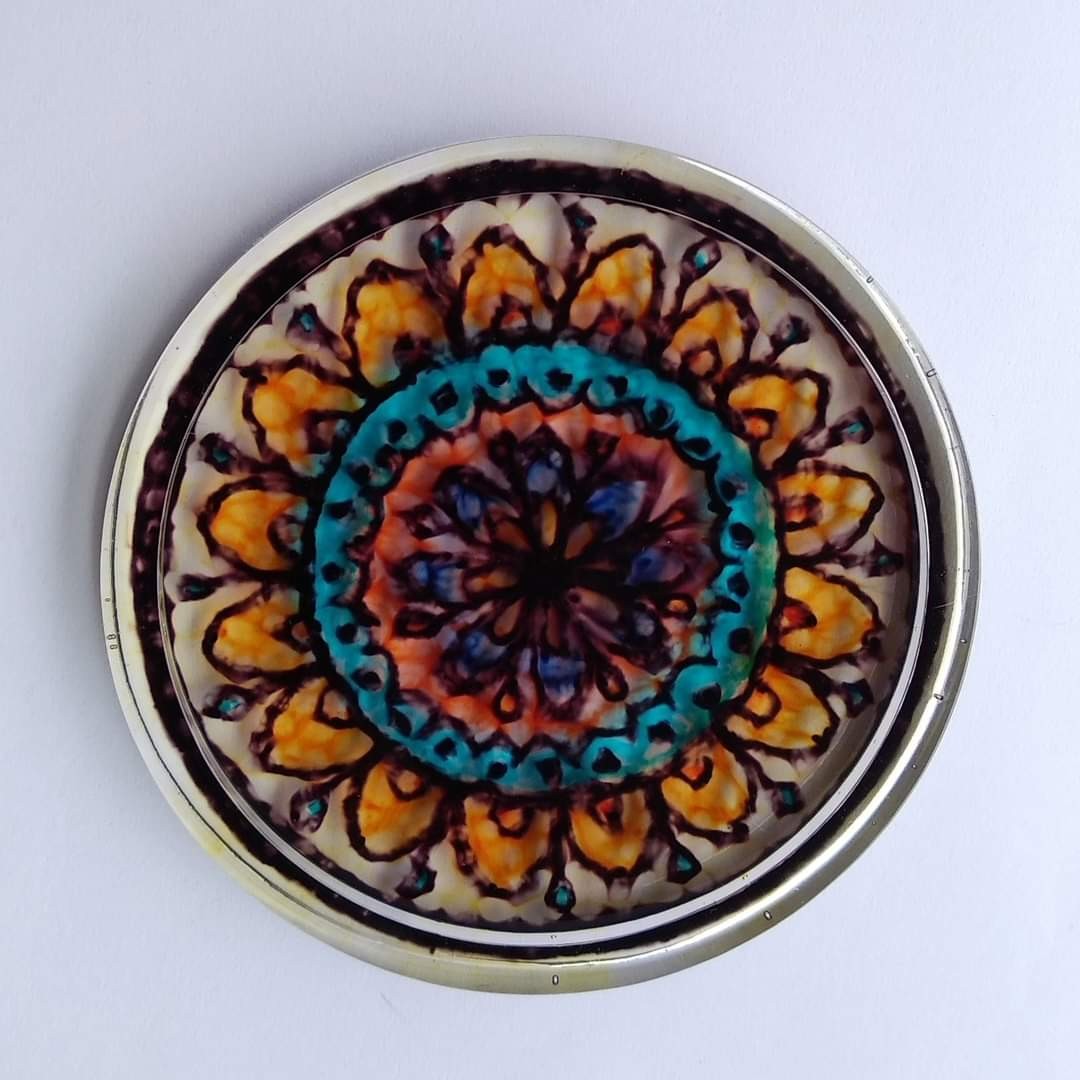 Round resin piece set in a tin lid — hand-drawn mandala with orange petals, teal inner ring and dark background