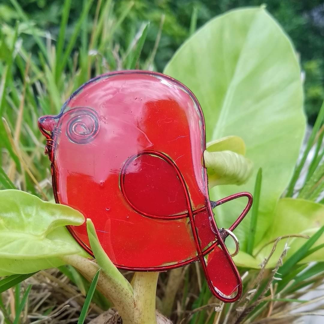 Red wire-and-resin chubby bird pendant nestled among lotus or taro leaves in a garden setting