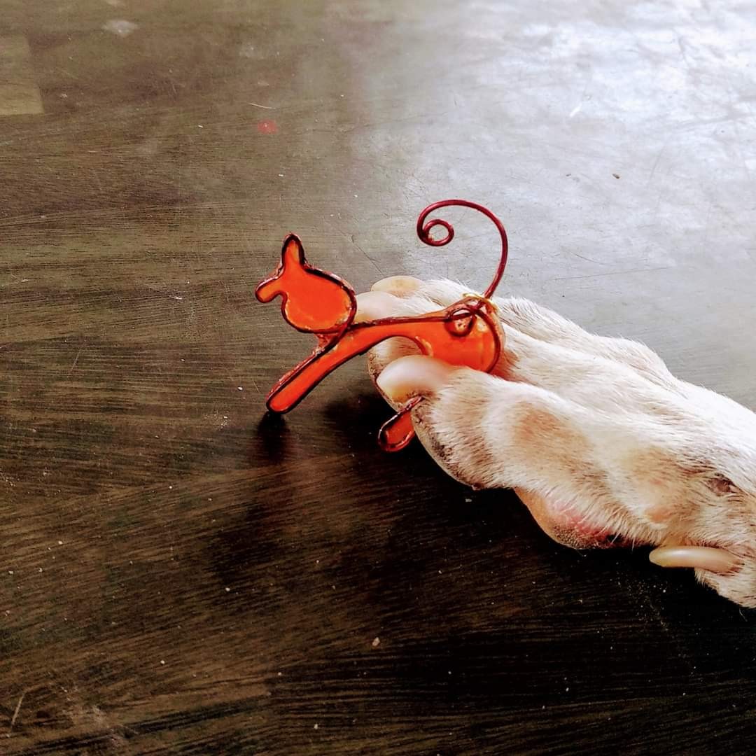 Orange wire-and-resin cat figurine/pendant resting on a dog's paw — playful juxtaposition