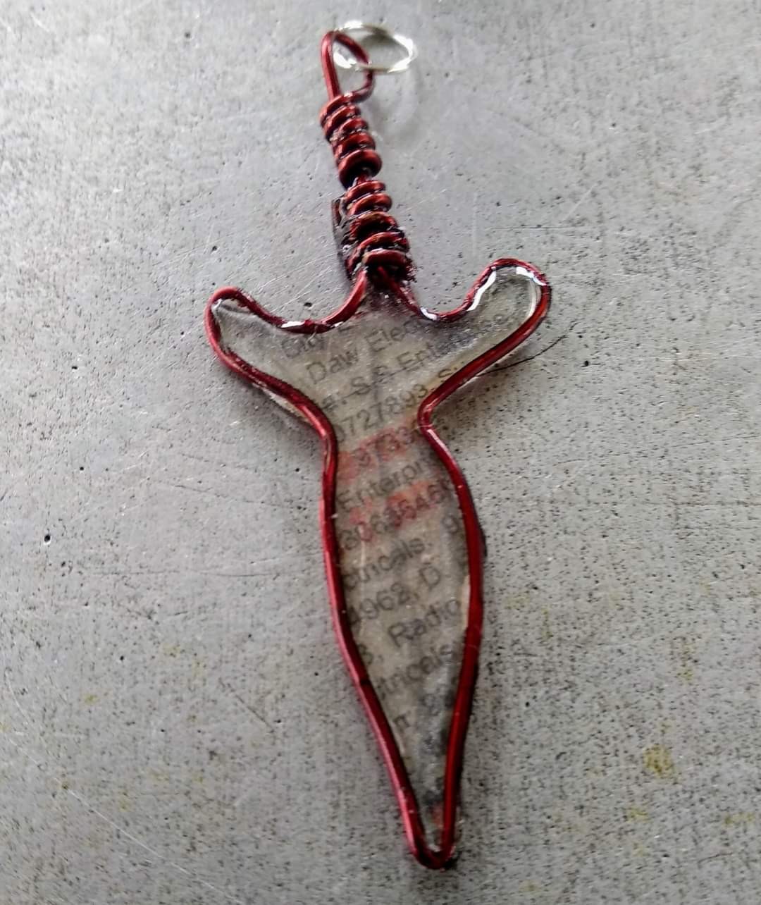 Wire-and-resin dagger pendant — clear resin body with newsprint embedded, red wire frame and wrapped hilt