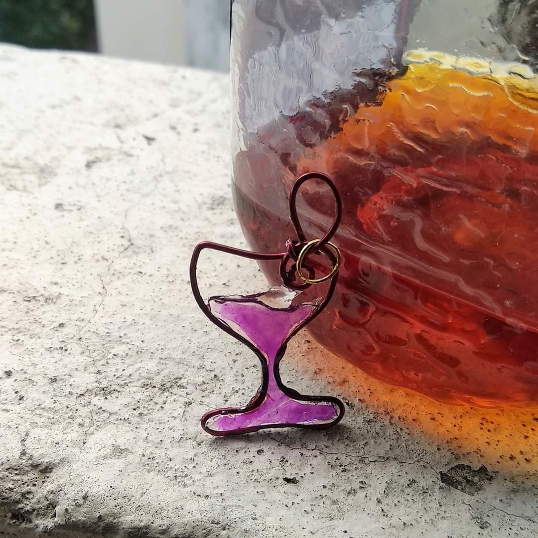 Wire-and-resin cocktail goblet pendant in purple resin with copper wire frame, leaning against a large amber resin sphere