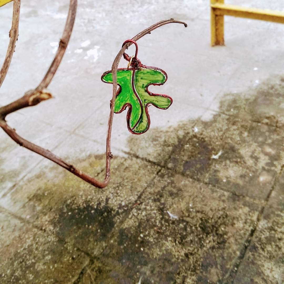 Wire-and-resin green oak leaf pendant hanging from a bare twig — copper wire outlines the leaf shape, green resin fill