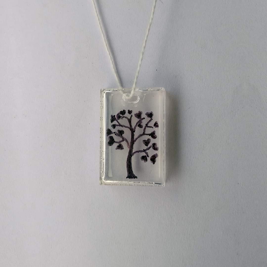 Clear rectangular resin pendant on a string — hand-drawn tree-of-life silhouette embedded inside