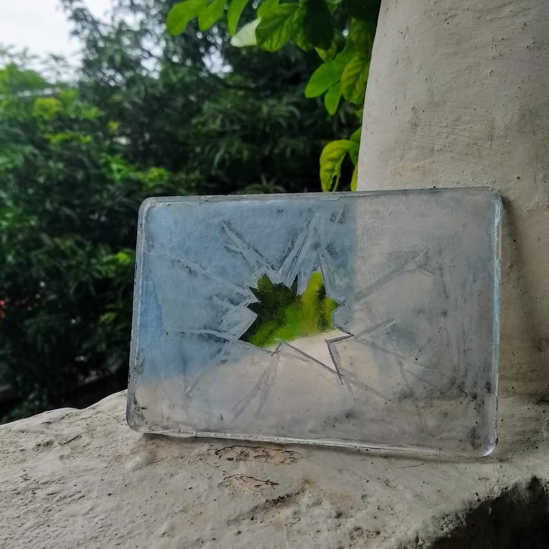 Rectangular clear resin slab on a concrete ledge outdoors — green maple leaf embedded at centre, surrounded by an icy cracked-ice texture