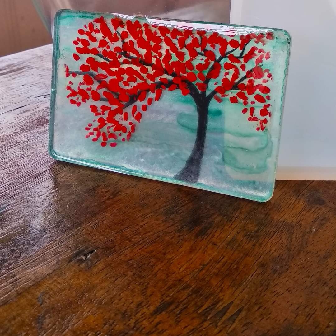 Rectangular resin tray with a hand-painted red tree on turquoise background, standing upright on a wooden table